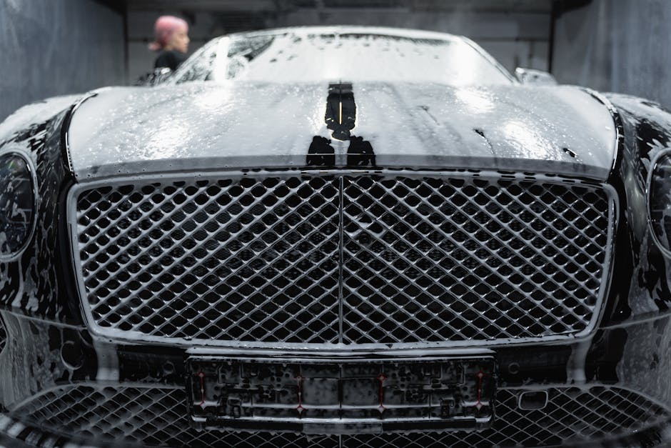 A close-up of a luxurious black car being cleaned with foamy soap at a carwash.