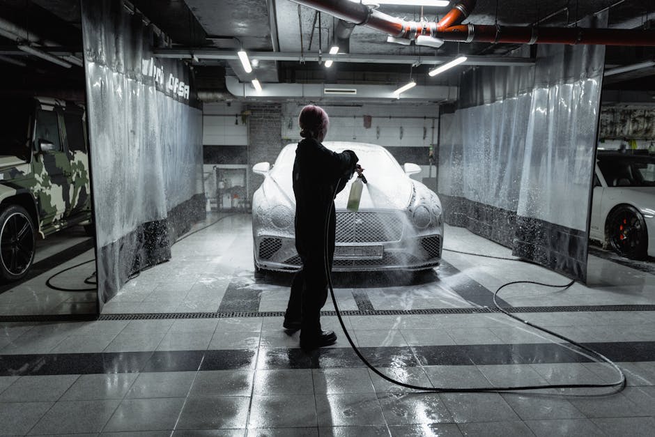 A person using a hose to spray a car with snow foam in an indoor carwash setting.